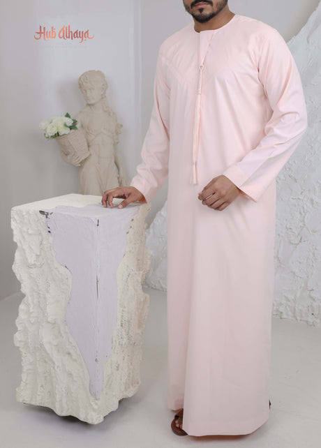 Man wearing a light pink traditional outfit sitting on a white chair with a neutral background.
